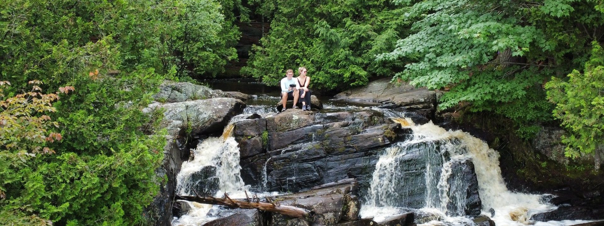 Couple sitting at a waterfall, surrounded by lush greenery, enjoying the stunning natural scenery.
